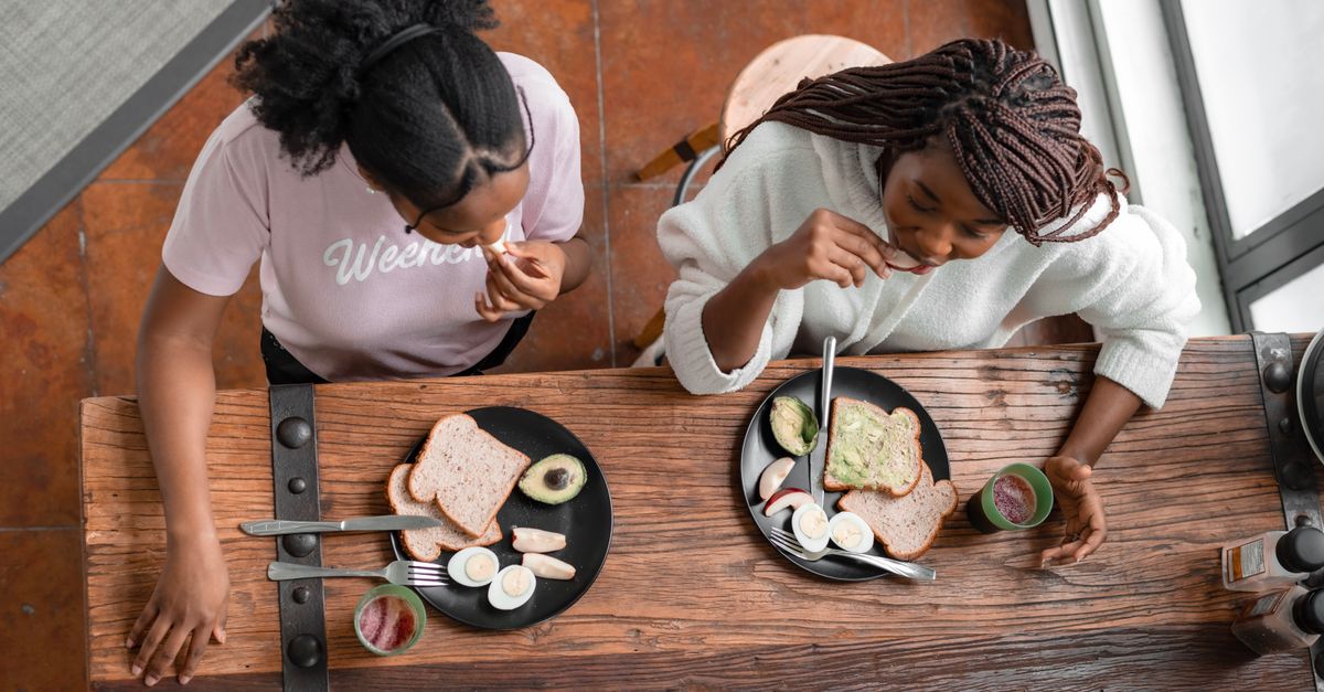 Two women eating a healthy breakfast with toast, avocado, and fruit.